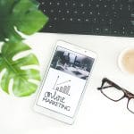 A smartphone with the word online marketing on it next to a keyboard and glasses.